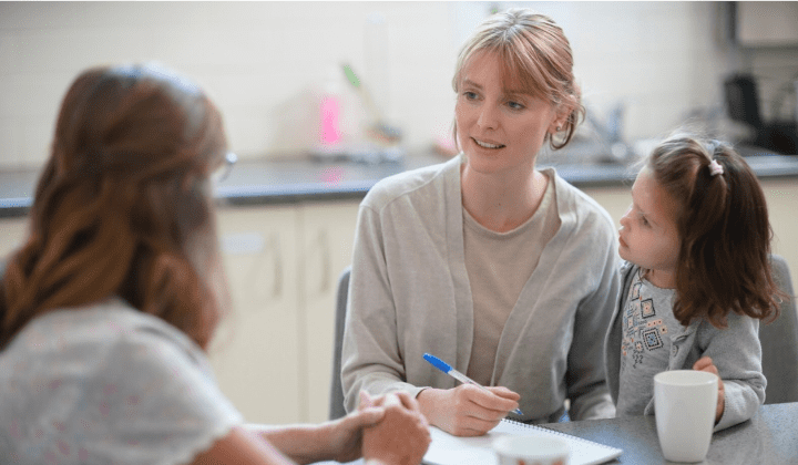 Light skin woman sitting with young daughter talking to a support worker about safety tips.