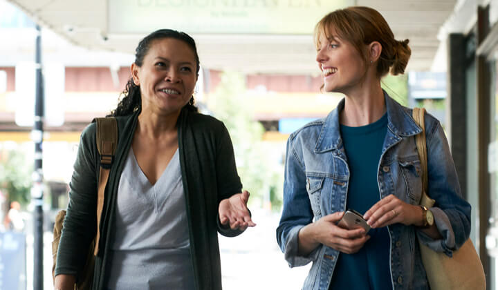 One light and one brown skin woman walking in conversation.