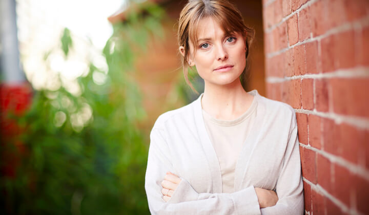 Light skin woman with arms crossed standing next to a red brick wall.