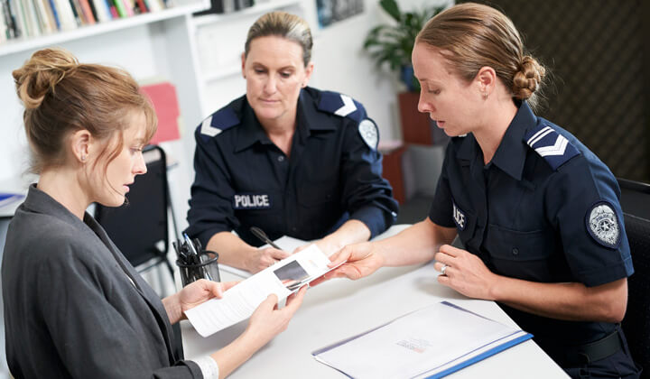 Light skin woman seeking help who is communicating with two light skin policewomen about her domestic and technology facilitated abuse situation.